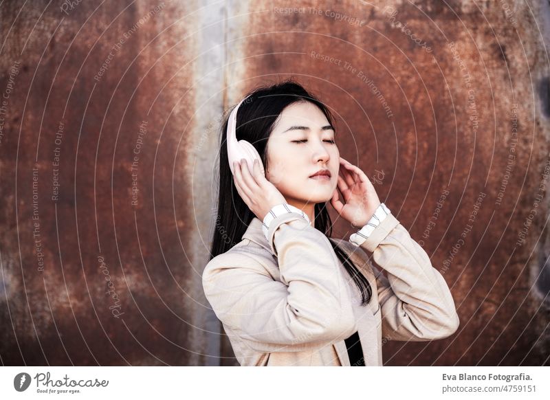 entspannte Geschäftsfrau mit geschlossenen Augen, die mit Kopfhörern und Mobiltelefon in der Stadt Musik hört Augen geschlossen Chinesisch Frau Großstadt Handy