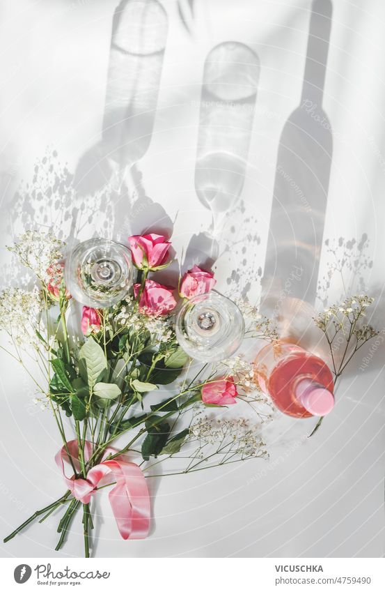 Rose Weinflasche mit Weingläsern und schönen Blumenstrauß mit Rosen auf weißem Hintergrund mit natürlichem Sonnenlicht Rosenwein Flasche weißer Hintergrund
