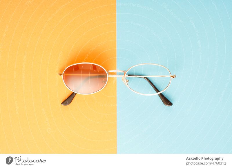 Defekte Sonnenbrille mit fehlendem Glas auf blauem und orangem Hintergrund. Zubehör Accessoire Nahaufnahme Konzept kreativ fehlerhaft Design Auge Brille