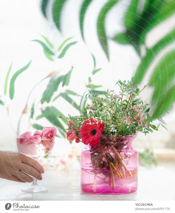Frauen Hand hält Champagnerglas mit Rosenblättern und Blume Eiswürfel auf dem Tisch mit Blumenstrauß in rosa Glasvase Beteiligung Sektglas Roséwein
