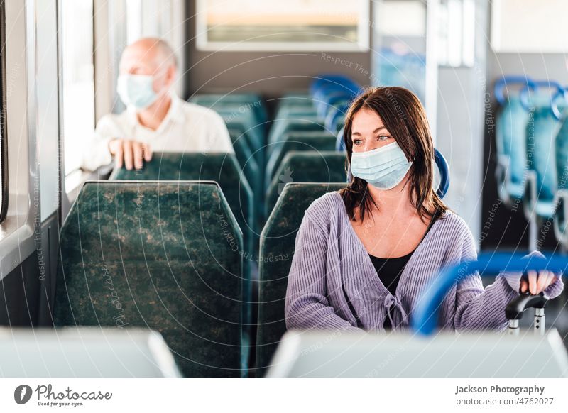 Ernste Fahrgäste mit Schutzmasken während ihrer Zugfahrt Mundschutz Pendler Passagier ernst traurig deprimiert nachdenklich Gepäck sitzen Sitz im Inneren