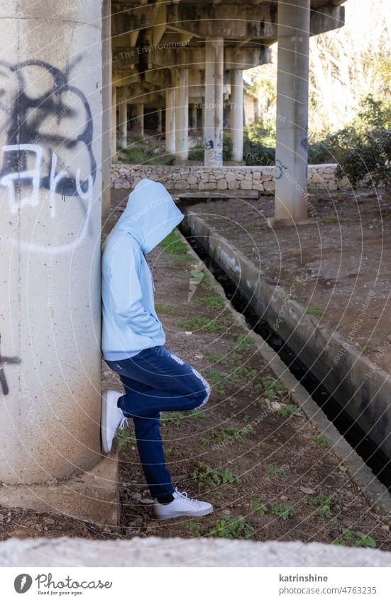 Kapuzenpulli Teenager-Mädchen in hellblauem Oversize-Kapuzenpulli bleibt unter Brücke hell-blau Jugendzeit Übergröße Jeanshose im Freien Brückenpfeiler Graffiti