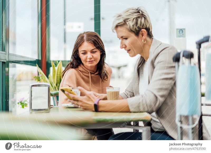 Zwei reisende Freundinnen genießen die Zeit in einem Cafe - Maske und Gepäck im Vordergrund Mundschutz Frauen Café warten Telefon Transport Erwachsener