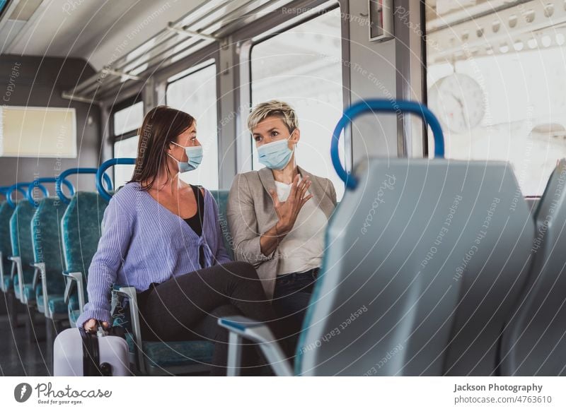 Ein befreundetes Paar trägt eine Maske und unterhält sich während einer Zugfahrt reisen Mundschutz Frau sich[Akk] unterhaltend reden Talkrunde Frauen Mann