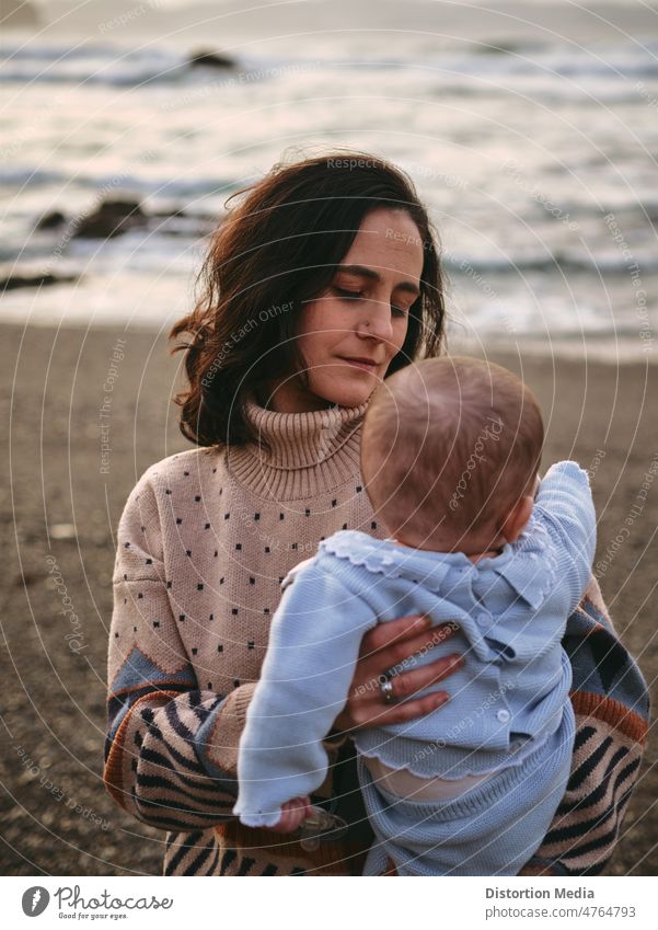 Junge Mutter schaut liebevoll und zärtlich auf ihr Baby am Strand, vertikal Töchter bezaubernd Kaukasier verbindlich liebend Einheitskommunikation