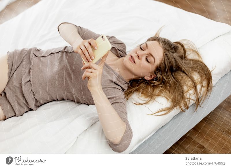 Junge Frau im Bett am Morgen, die soziale Netzwerke auf ihrem Smartphone überprüft Schlafzimmer Pyjama im Innenbereich Lifestyle Nachricht Lügen Erwachsener