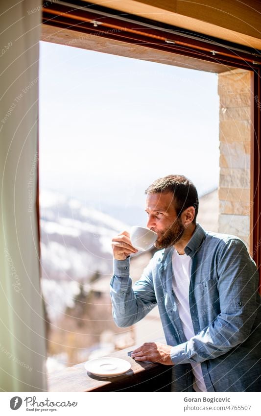 Junger Mann mit einer Tasse heißem Tee am Winterfenster Appartement attraktiv schön Getränk Windstille Kaffee niedlich trinken genießend Gesicht heimwärts Hotel