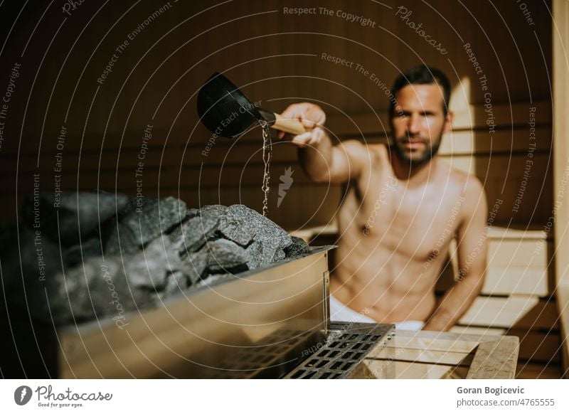 Junger Mann gießt Wasser auf einen heißen Stein in der Sauna erwärmen jung Verdunstung Spa Gesundheit Behandlung Schönheit Holz Bad Bank Therapie Erholung nass