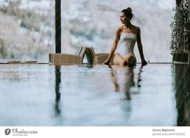 Attraktive junge Frau im Bikini sitzt am Beckenrand des Hallenbades Winter Spa sich[Akk] entspannen Erholung Pool schön Schwimmsport Wellness Resort Lifestyle