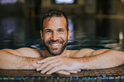 Porträt eines lächelnden jungen Mannes, der sich am Rande des Schwimmbads entspannt Junger Mann gutaussehender Mann hübscher junger Mann Beckenrand männlich