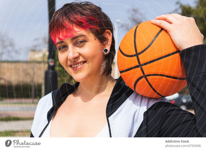 Positive Dame mit Basketball auf der Straße Sportlerin Lächeln Spieler Streetball Ball positiv Porträt Frau Lifestyle gefärbtes Haar Gerät Hobby Wellness
