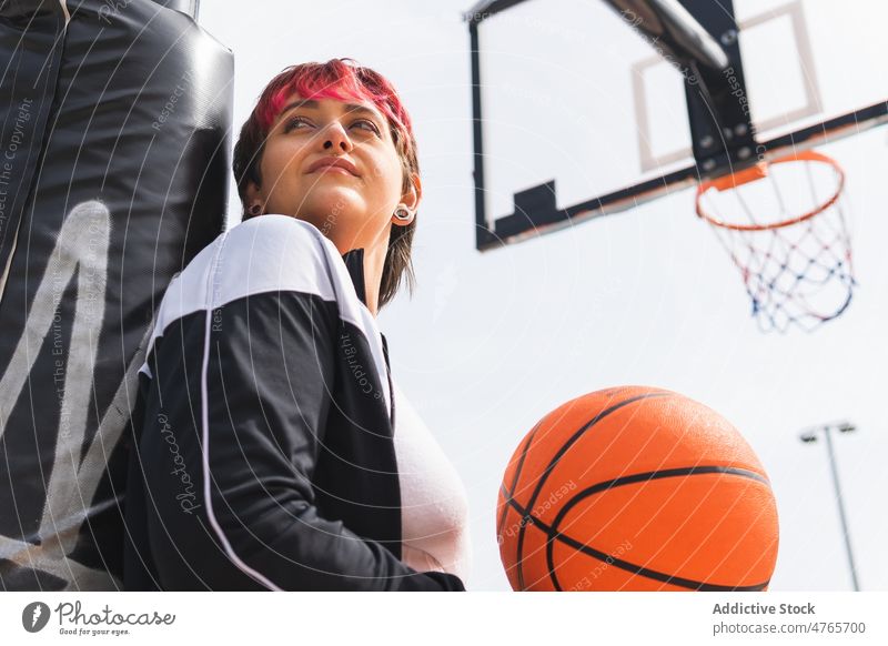 Nachdenkliche Frau mit Ball auf Basketball-Sportplatz Sportlerin Spieler verträumt Streetball Denken Reifen spielen Himmel üben Training Aktivität Lifestyle