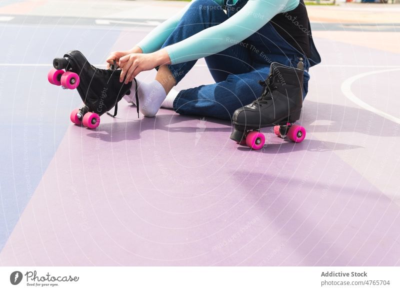 Anonyme Frau beim Anziehen von Rollschuhen auf einem Sportplatz Rollerskate Vierfachrolle Schlittschuh sportlich üben Hobby Lifestyle aktiv Sportpark Training