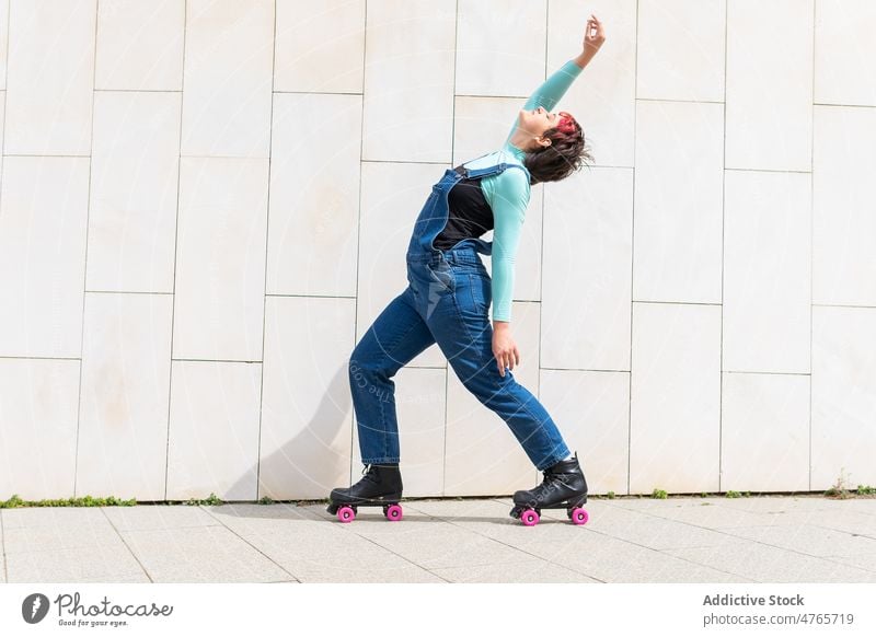 Frau in Rollschuhen tanzt in der Nähe eines Gebäudes auf der Straße Vierfachrolle Rollerskate Tanzen Schlittschuh Hobby Straßenbelag Wand sportlich sorgenfrei