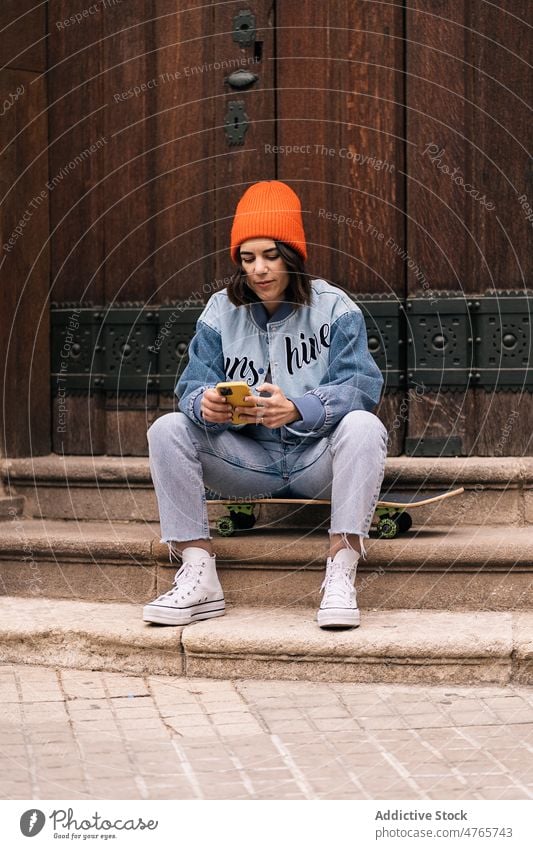 Frau, die in der Nähe eines Gebäudes auf einem Mobiltelefon surft Textnachricht Skateboard Straße Browsen Streetstyle Großstadt urban Hobby Vorschein Stadt