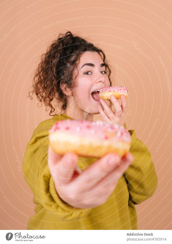 Glückliche Frau, die süße Donuts isst und in die Kamera schaut essen geben Dessert genießen Geschmack teilen lecker Zuckerguß Leckerbissen hungrig zuckerhaltig