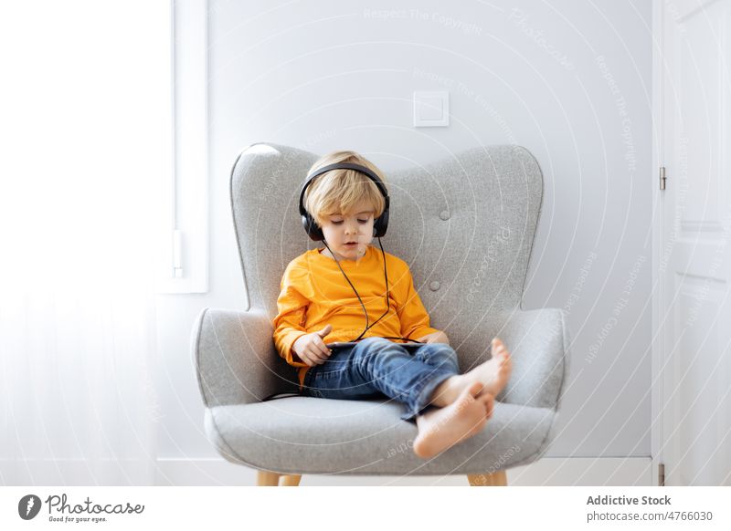 Barfuß Junge in Kopfhörer beobachten Cartoons auf Tablet Tablette Karikatur zuschauen zuhören benutzend Süchtige digital Internet freie Zeit heimwärts Armsessel