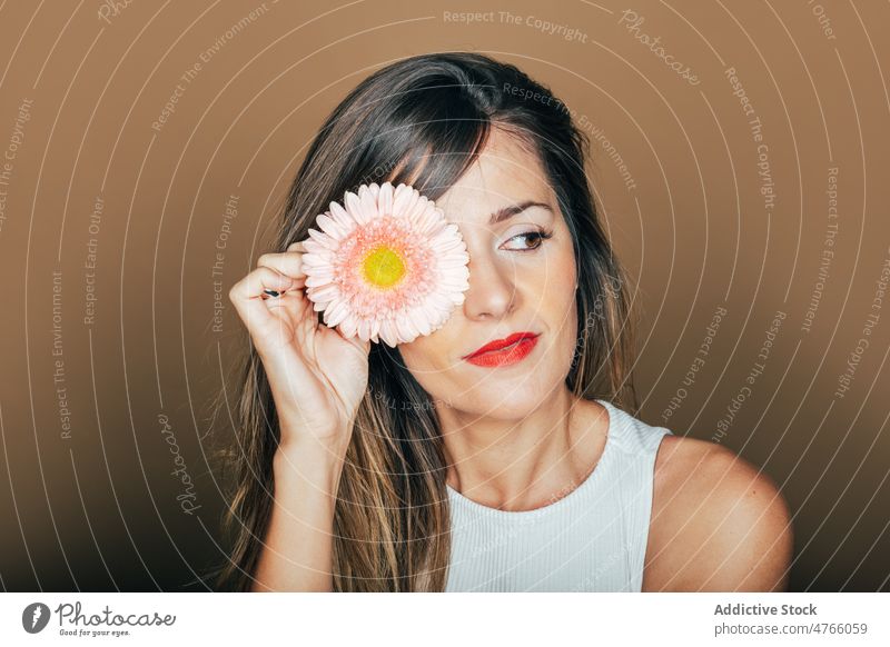 Frau bedeckt Auge mit Gerbera-Blume im Atelier Model filigran Porträt sanft rosa Stil Angebot rote Lippen Augen abdecken natürlich feminin romantisch charmant
