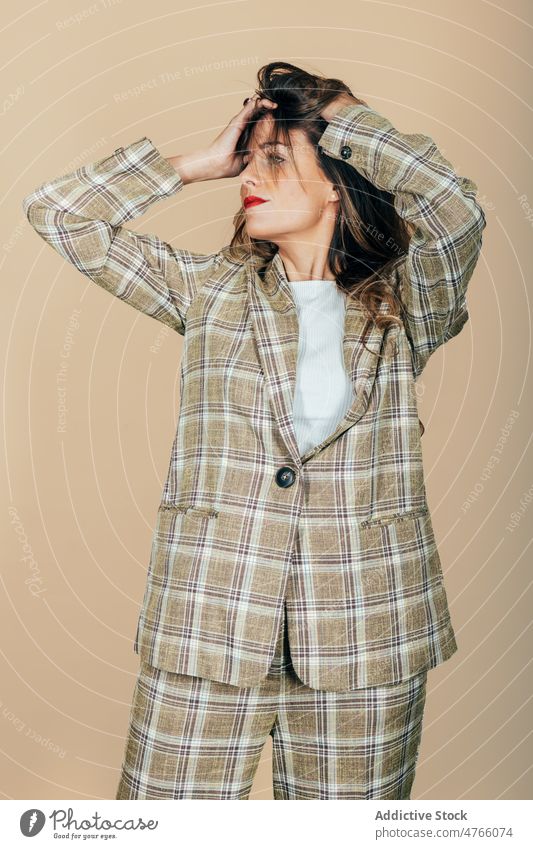 Stilvolle Frau im Anzug, die ihr Haar im Studio zerzaust Model Haare kräuseln kariert Haare berühren trendy selbstbewusst cool Vorschein Zeitgenosse
