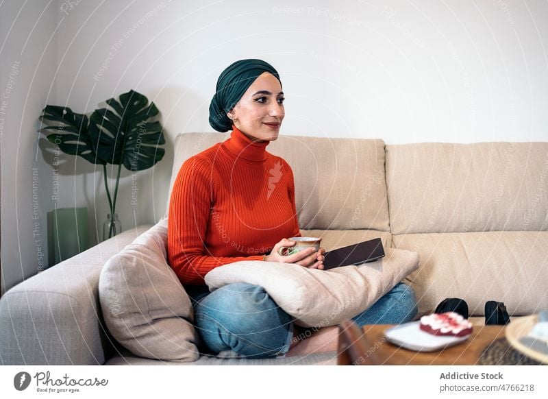 Muslimische Frau nippt an einem heißen Getränk Porträt Heißgetränk Tee ruhen Sofa Wochenende heimwärts Wohnzimmer tagsüber muslimisch ethnisch Islam Liege