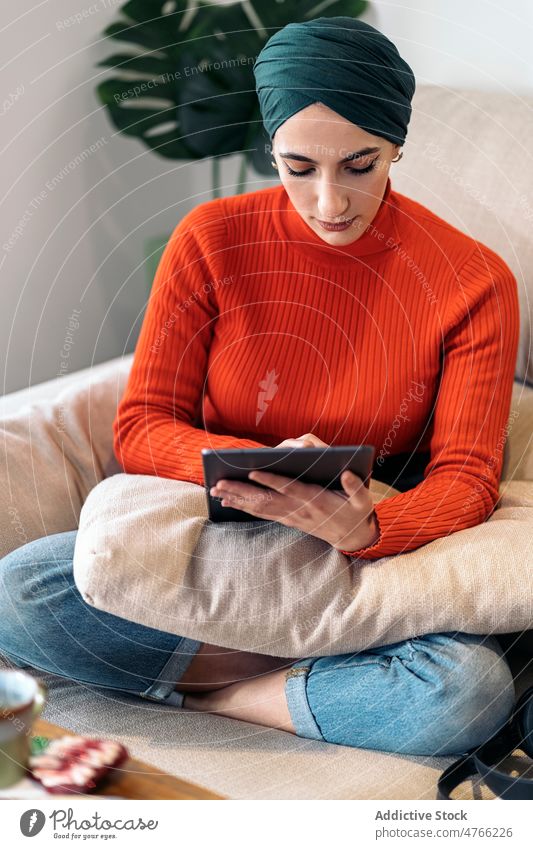 Muslimische Frau mit Tablet auf der Couch Porträt Tablette benutzend Sofa heimwärts Wohnzimmer soziale Netzwerke ruhen Wochenende online muslimisch ethnisch