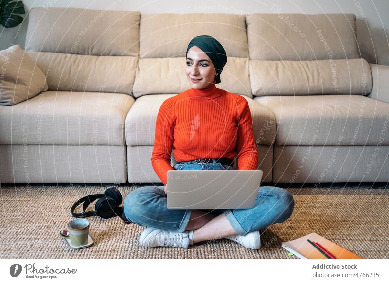 Freiberuflerin arbeitet auf dem Boden Frau Porträt muslimisch Laptop benutzend freiberuflich heimwärts ethnisch Kopftuch Tippen Stock Islam Telearbeit sitzen