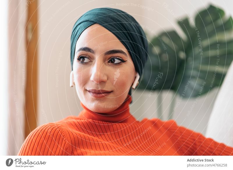 Muslimische Frau hört Musik auf dem Sofa Porträt muslimisch zuhören benutzend Kopfhörer Ohrstöpsel tws Drahtlos heimwärts ruhen soziale Netzwerke Wochenende