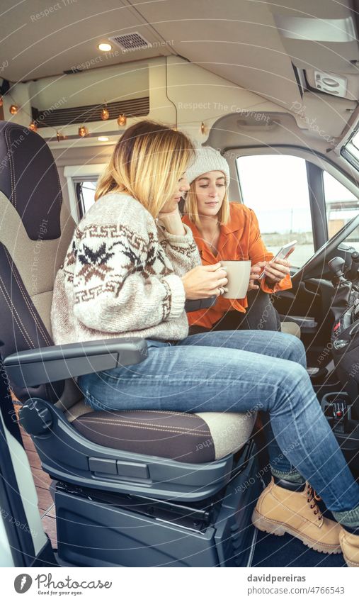 Frauen mit einem Handy im Kaffee-Look auf dem Vordersitz eines Wohnmobils Sitzen Kleintransporter trinken Blick Mobile Winter Morgen Tür öffnen Freunde