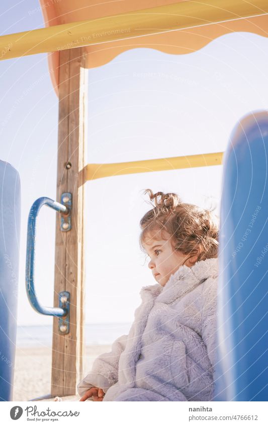 Kleines Mädchen genießt einen sonnigen Wintertag auf dem Spielplatz spielerisch Baby Kleinkind Park Sliden lockig Spanisch Europäer bezaubernd lieblich Kindheit