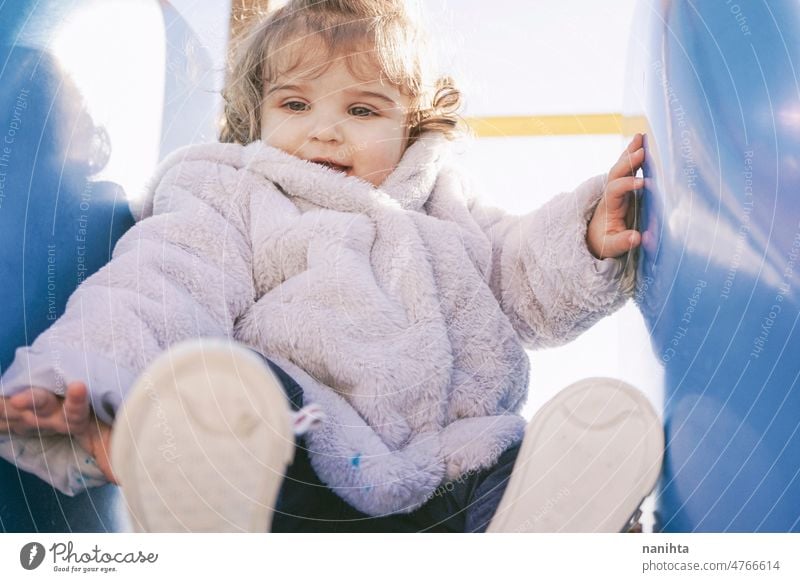 Kleines Mädchen genießt einen sonnigen Wintertag auf dem Spielplatz spielerisch Baby Kleinkind Park Sliden lockig Spanisch Europäer bezaubernd lieblich Kindheit