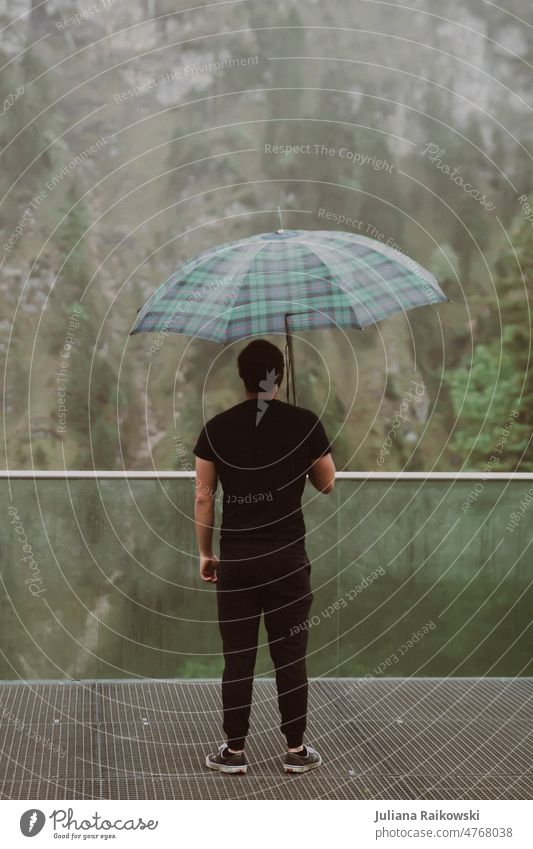 Mann steht im Regen mit Regenschirm Mensch Wetter schlechtes Wetter Außenaufnahme Farbfoto Tag nass Klima Schirm Schutz kalt Gedeckte Farben Umwelt kariert grau