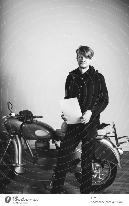 ein Mann mit weißen Blatt steht an einem alten Motorrad im Studio Studioaufnahme MZ s/w Trzoska Schwarzweißfoto b/w Tag b&w ruhig Berlin blond