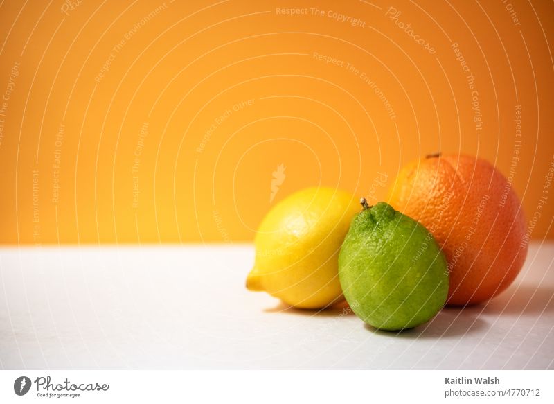 Frische Zitrusfrüchte: Zitrone, Limette und Orange mit kräftigem orangefarbenem Hintergrund Frucht Kalk Gesundheit Vitamin Lebensmittel Ernährung gelb grün