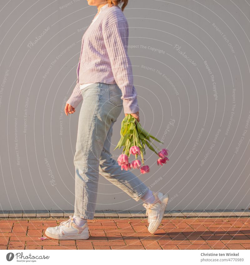 Schwungvoll in den Montag... Eine junge Frau mit einem Strauß Tulpen in der Hand läuft vor einer hellen Wand entlang laufen schwungvoll Blumenstrauß Frühling