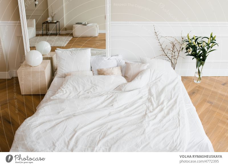 Ein Doppelbett mit weißer Bettwäsche und beigen Kissen in einem hellen skandinavischen Schlafzimmer, ein Bett auf dem Boden und Blumen in einer Vase Möbel