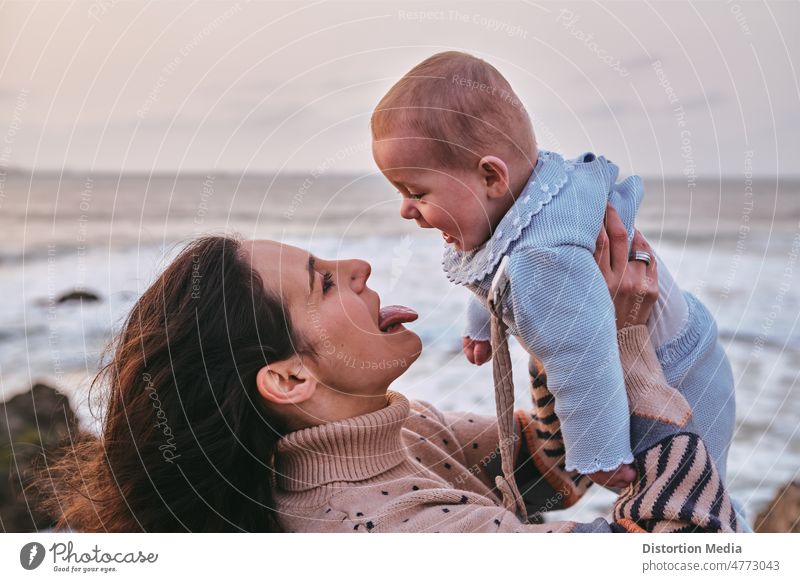 Alleinstehende junge Mutter, die ihren kleinen Sohn im Arm hält. Sie spielen und sie streckt ihre Zunge heraus, während er lächelt Mutter und Baby Glück