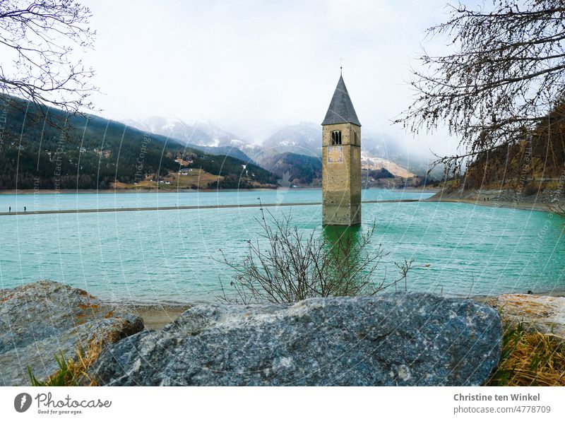 Der versunkene Kirchturm der Pfarrkirche von Alt-Graun im sehr leeren Reschensee in Südtirol. Die beiden Spaziergänger auf der Sandbank machen gerade ein Erinnerungsfoto