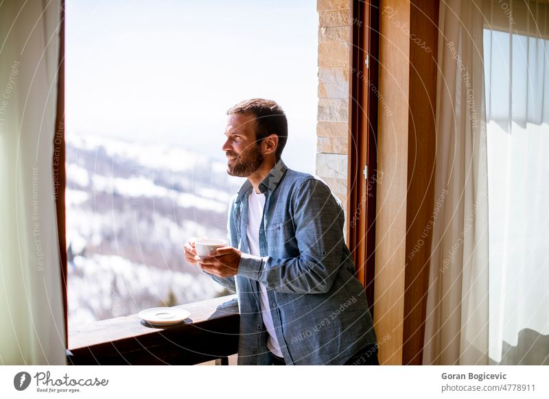Junger Mann mit einer Tasse heißem Tee am Winterfenster Appartement attraktiv schön Getränk Windstille Kaffee niedlich trinken genießend Gesicht heimwärts Hotel