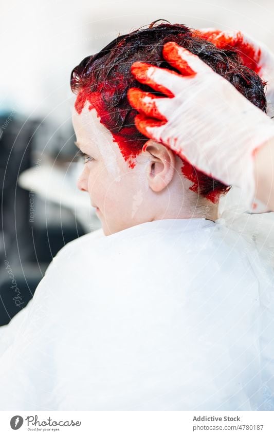 Unkenntlich gemachter Friseur, der einem Jungen die Haare färbt Kind Salon Meister rote Haare gefärbtes Haar Vorschein Frisur informell Stil Klient trendy Licht