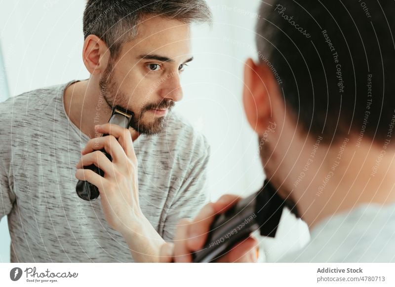 Mann rasiert Bart mit Trimmer Vollbart Rasieren Routine unrasiert Spiegel Hygiene täglich Bad Reflexion & Spiegelung heimwärts Vorschein männlich Licht Typ