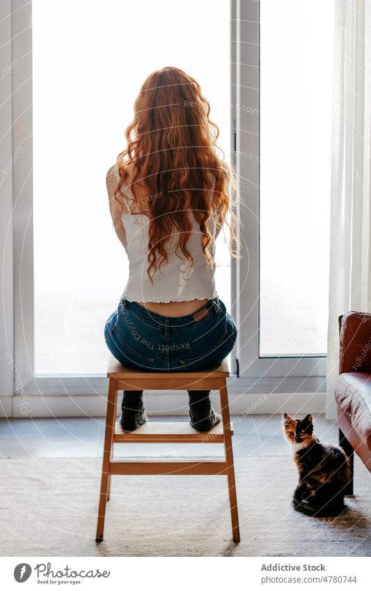 Anonyme rothaarige Frau, die am Fenster sitzt einsam Einsamkeit Raum Wohnzimmer beobachten Stil Innenbereich Design krause Haare heimisch Appartement rote Haare