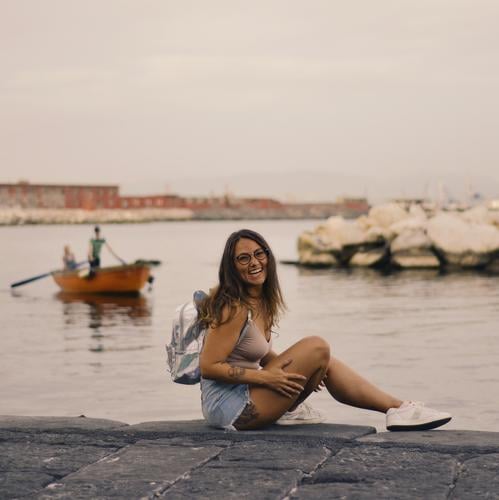Junge hübsche Frau sitzt allein auf dem Pier in der Nähe des Meeres, lächelnd und lachend Rücken Hintergrund Strand schön Windstille Großstadt Abend Freiheit