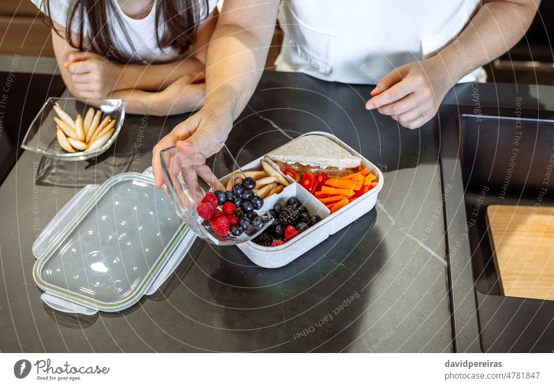 Mädchen beobachtet ihre Mutter setzen Essen in ihre Lunch-Box unkenntlich Setzen Frucht gesunder Snack Tochter organisch Blick Schule Veganismus vorbereitend
