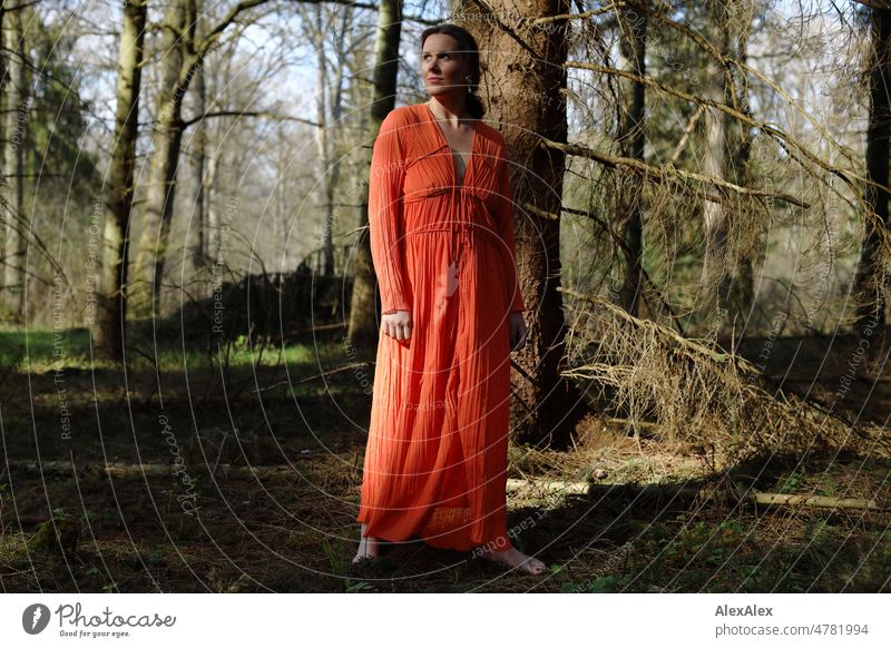 Junge Frau in rotem Kleid steht im Frühlingswald und posiert für die Kamera jung schön langhaarig brünett anmutig Schönheit 18-30 Jahre selbstbewußt authentisch