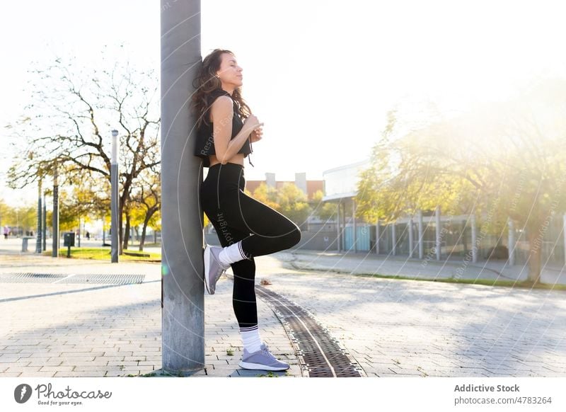 Sportliche Frau mit Pause in der Nähe des Pfostens auf der Straße Sportlerin Athlet ruhen Training pausieren Großstadt Läufer Gesunder Lebensstil Sportkleidung
