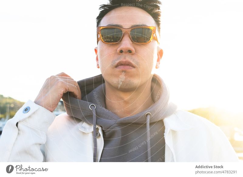 Stilvoller Mann mit Sonnenbrille auf der Straße Vorschein Großstadt trendy Mode selbstbewusst Accessoire Kapuzenpulli männlich Sonnenlicht ernst Sonnenschein