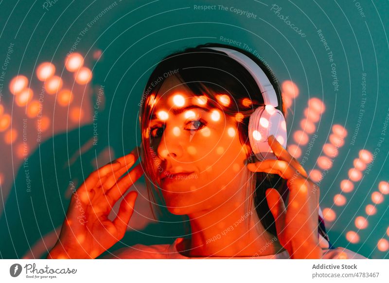 Charmante Frau mit Kopfhörern unter Lichtern Musik Stil Gesang meloman Hobby glühen Melodie zuhören Porträt Atelier Klang kreativ Audio Dame modern