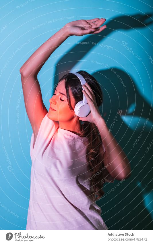 Frau hört Musik in einem Studio mit Lichtern Kopfhörer Stil rot Gesang erhobener Arm meloman unterhalten Hobby Melodie trendy zuhören Atelier farbenfroh Klang