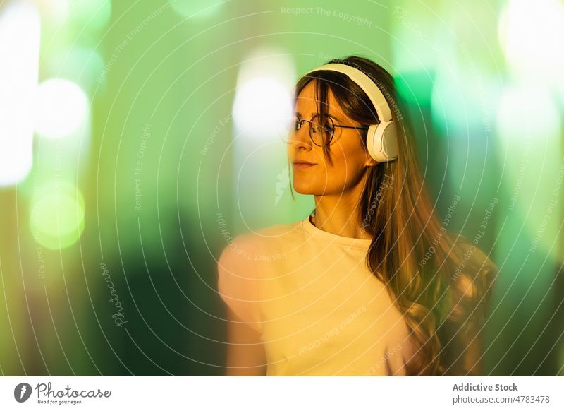 Frau hört Musik unter Lichtern Kopfhörer Stil Gesang meloman trendy Hobby Melodie zuhören Atelier farbenfroh Klang lebhaft Brille kreativ Audio hell Farbe Dame