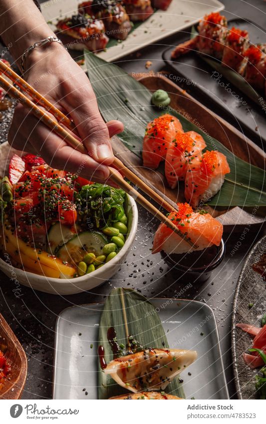 Anonyme Person isst asiatisches Essen in einem Restaurant Menschen essen Asiatische Küche sortiert Tisch Sushi stoßen jiaozi Udon Speise dienen Gastronomie